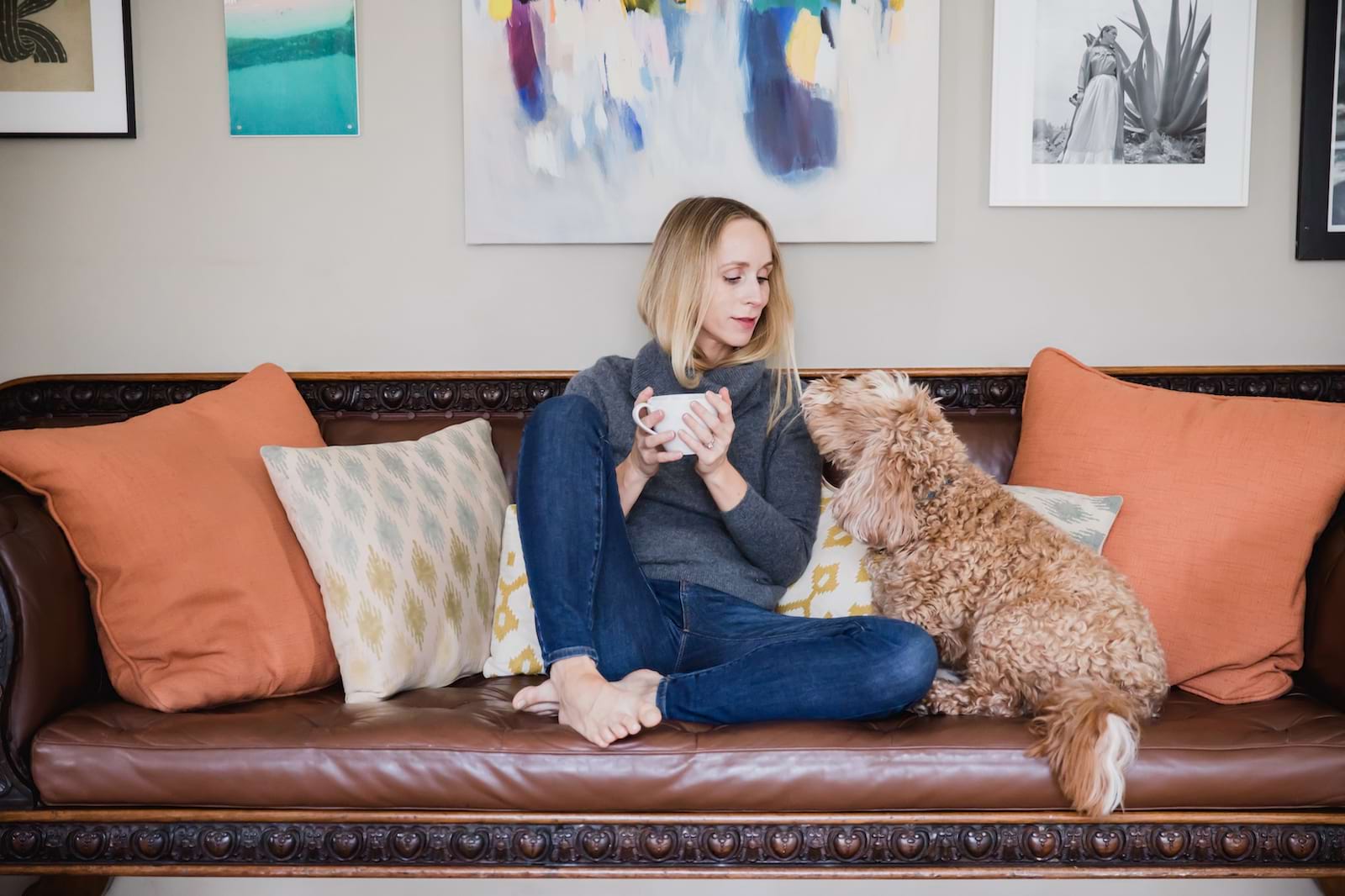 Image of a woman drinking coffee on her. sofa with her dog